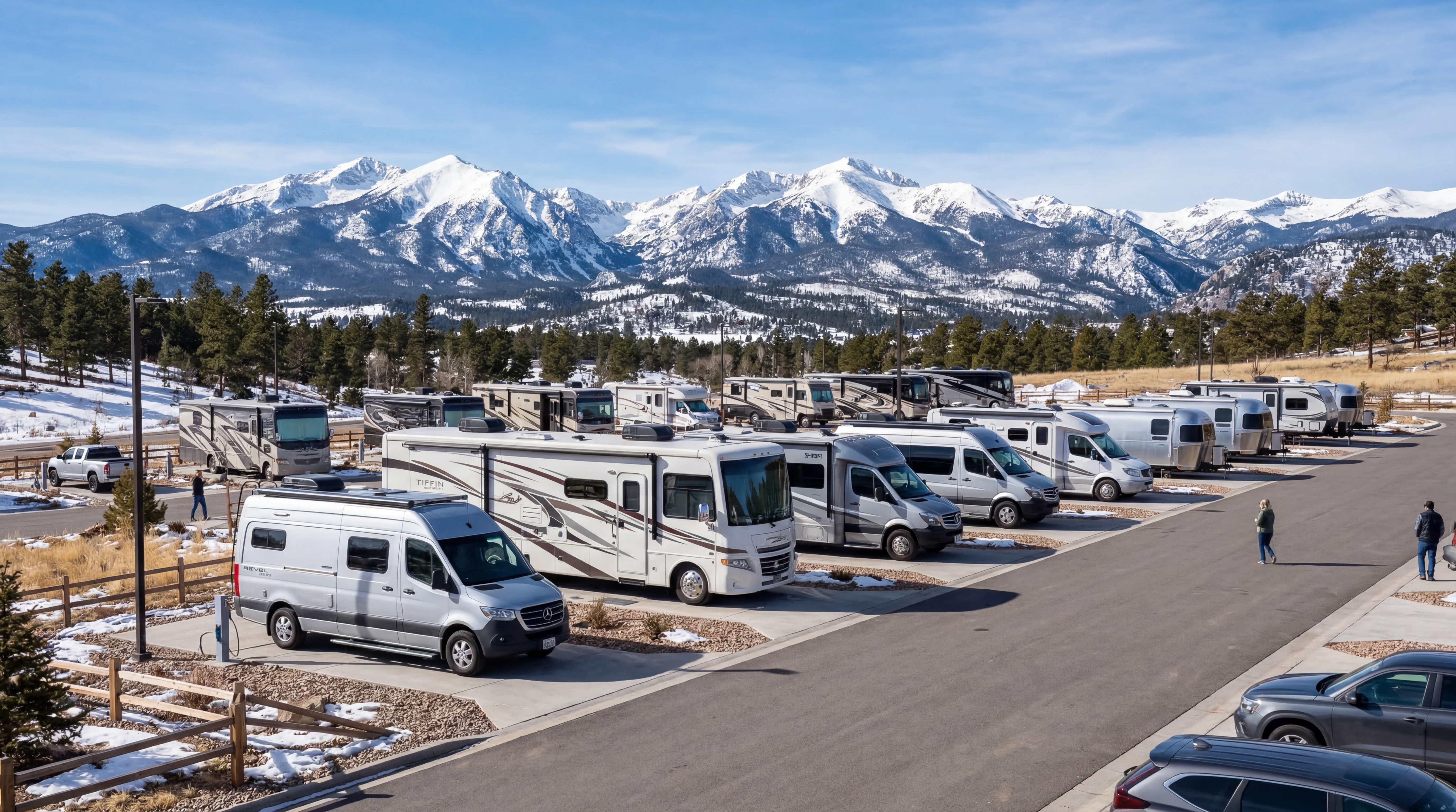 Modern RVs lined up in a Colorado lot with snow capped Rocky Mountains