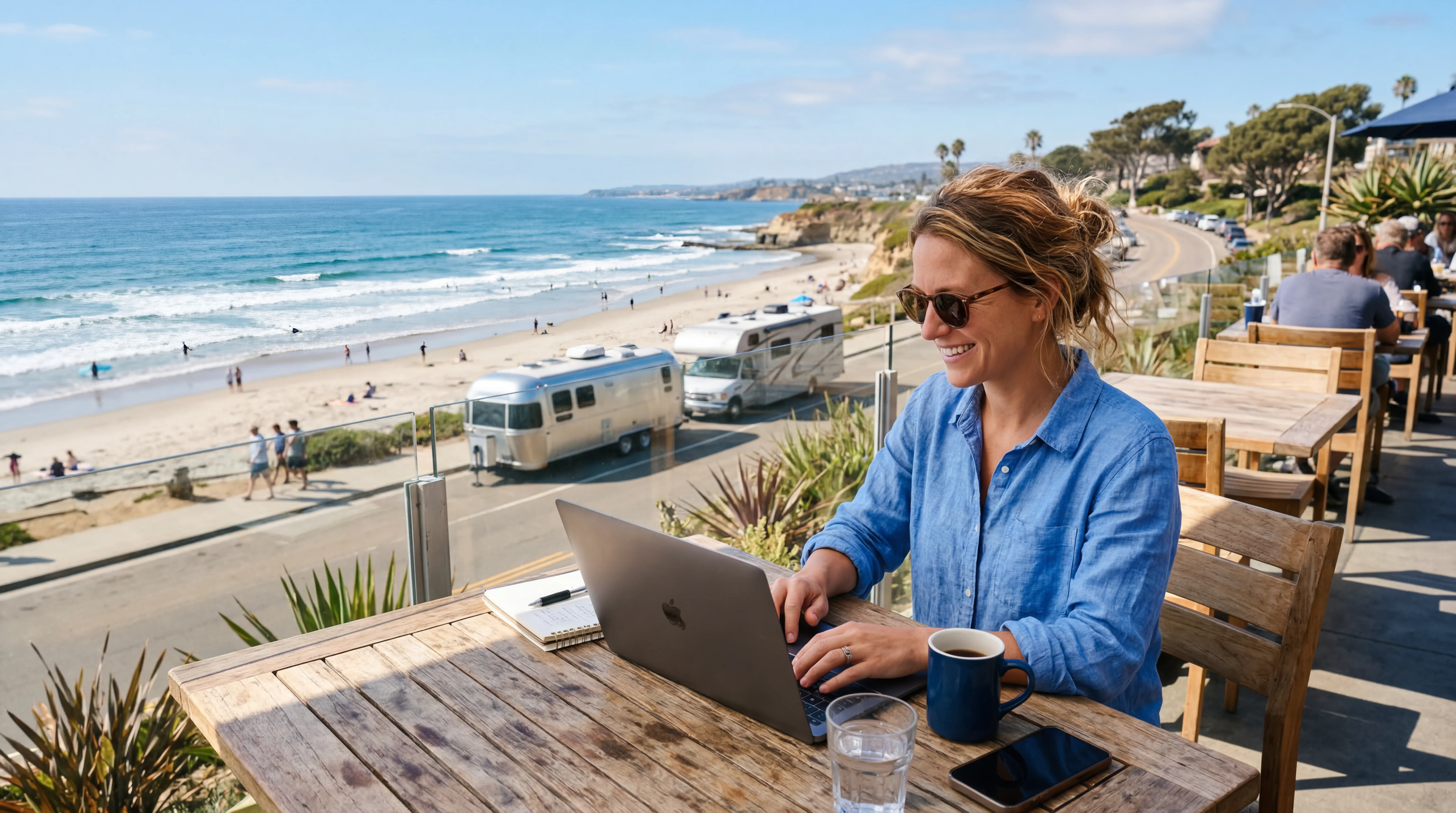 Person planning an RV trip on laptop at oceanfront table in San Diego