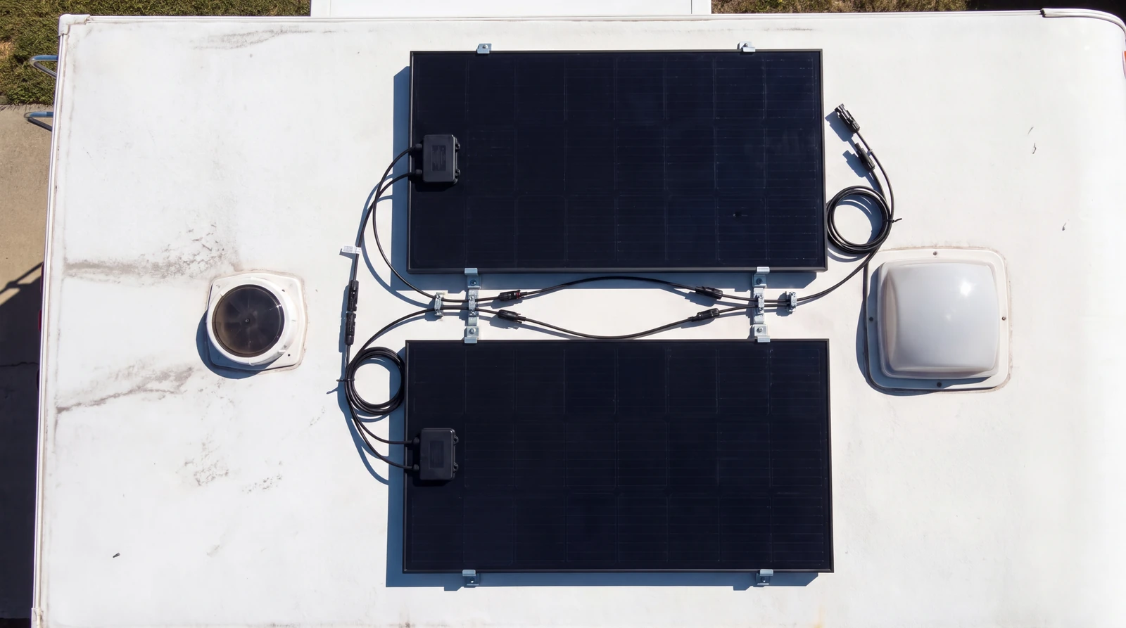 Overhead view of two rigid solar panels on a white RV roof with junction boxes and branch connectors joined by neat black wiring